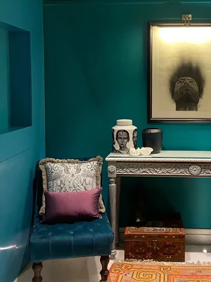 This corner is a celebration of color and curated decor. The deep green walls provide a dramatic backdrop for a uniquely carved silver console, a plush velvet wing chair, and various artifacts.
