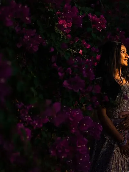 A portrait taken at sunset. The warm light hits the bride from the side, highlighting her smile as she stands against a backdrop of beautiful purple flowers.