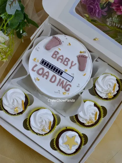 This bento cake and cupcake set was for a special baby shower. The design features a 'Baby Loading' theme on a mini choco-vanilla cake, surrounded by six matching cupcakes with simple white frosting and gold star details.