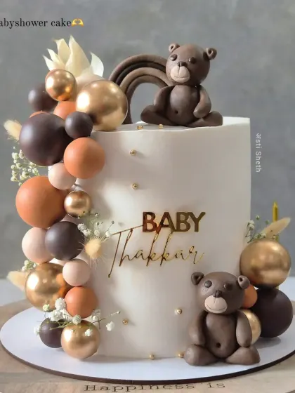 A neutral-toned baby shower cake with adorable, handcrafted teddy bears. The balloon cascade in shades of brown, beige, and gold creates a warm, modern look.
