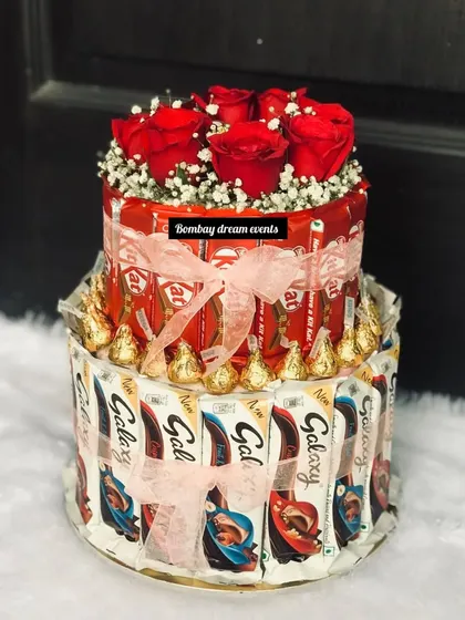 A two-tiered chocolate tower featuring KitKat and Galaxy bars, topped with fresh red roses. It's a unique alternative to a traditional cake for any chocolate lover.