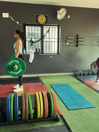 A client performs a deadlift, with a rack of colorful weight plates in the background, symbolizing the potential for progress.