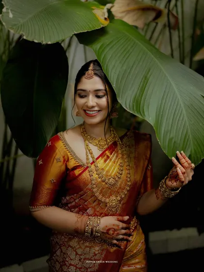A beautiful portrait of the bride, her smile radiant as she peeks from behind a large green leaf.