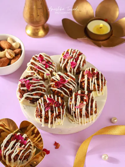 Mini granola and white chocolate bites decorated with rose petals, styled against a soft purple background.