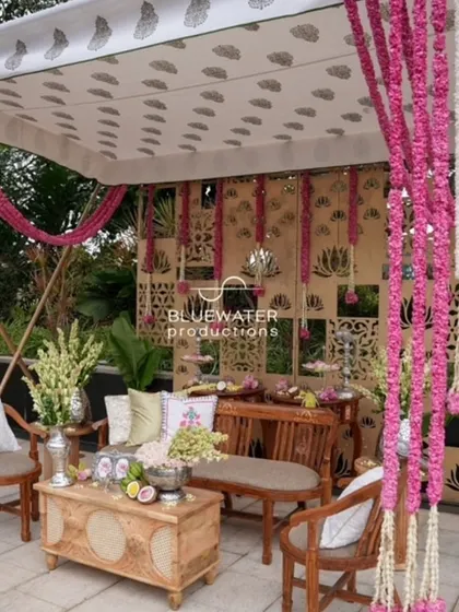 A traditional Haldi seating area with a canopy draped in floral garlands and a backdrop of intricate lotus-patterned screens.