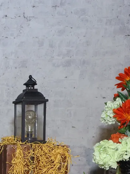 A simple yet effective decor detail for a food station. A classic black lantern, hay, and a small floral arrangement add a touch of rustic charm to the setup.