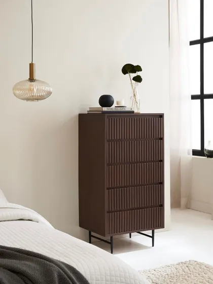 The tallboy chest of drawers placed in a serene bedroom context. The shot highlights its verticality and slim profile, making it suitable for various room sizes.