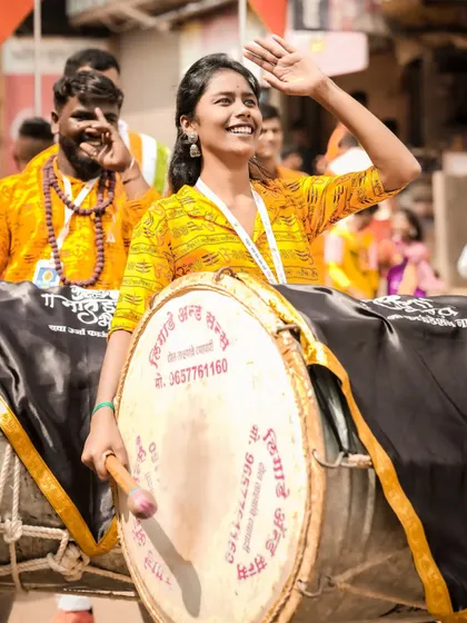 A candid black and white shot of a female dhol player, her smile lighting up the frame.