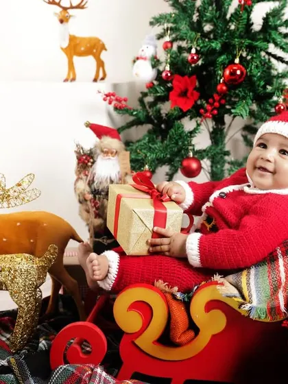 A happy baby Santa holding a gift. The genuine smile and festive props make this a perfect photo for sharing holiday joy.