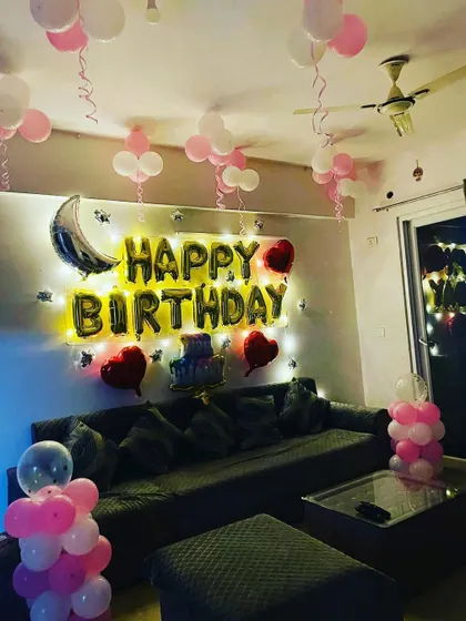 A simple and sweet birthday setup in a living room, with pink and white ceiling balloons and 'Happy Birthday' foil letters over the sofa.