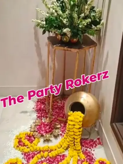 A creative entrance decor element for Teej, featuring a brass pot (kalash) from which marigold garlands and flower petals are spilling out.