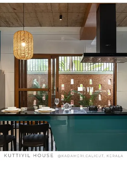 The kitchen at Kuttiyil House shows how a pop of color can transform a space. The glossy teal cabinetry contrasts with the patterned backsplash and exposed concrete ceiling, creating a modern kitchen that is both functional and full of personality.