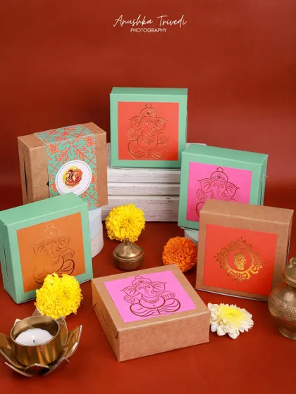 Colorful gift boxes with Ganesha motifs, perfect for Ganesh Chaturthi gifting, styled with marigold flowers and diyas.