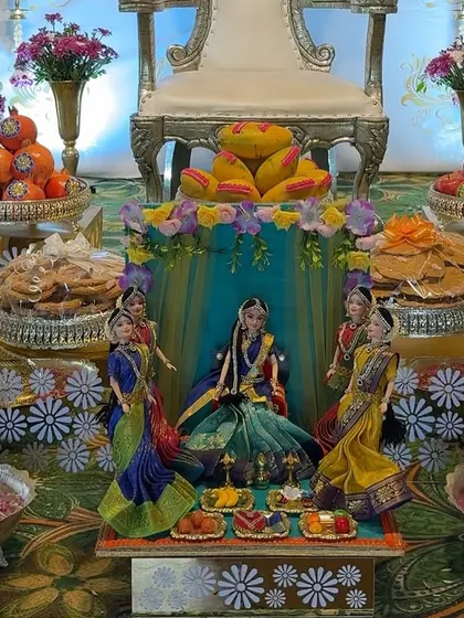 A close-up of a beautiful doll arrangement depicting a Seemantha ceremony. The dolls are surrounded by offering plates filled with traditional sweets and snacks.
