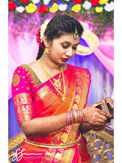 A candid shot of the bride during her engagement ceremony. Her makeup is classic and elegant, featuring a red lip and traditional gold jewellery that enhances her bridal glow.