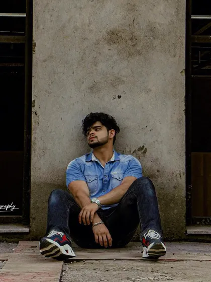 A full shot capturing a relaxed, contemplative pose against a concrete wall. The urban setting and casual styling make this a great addition to a street style portfolio.