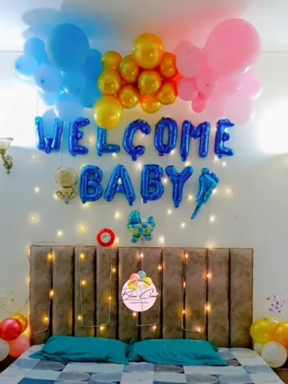 A colorful 'Welcome Baby' bedroom decoration with blue, pink, and gold balloons over the bed, complemented by fairy lights.