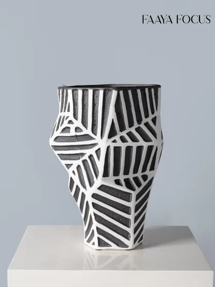 This geometric vase features a bold, hand-carved pattern of intersecting lines. The contrast between the black and white enhances its graphic quality, making it a striking accent piece for a modern interior.
