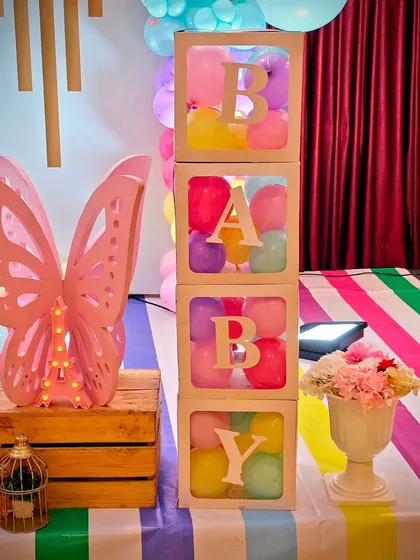 A close-up of the 'BABY' blocks and a light-up butterfly prop from the twins' party. The colorful striped tablecloth ties the whole theme together.