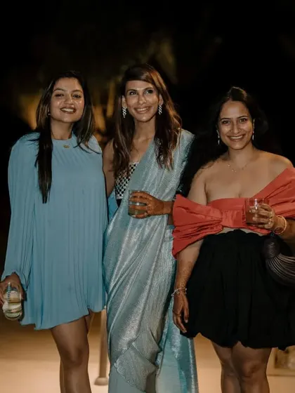 Friends and family gather for a photo at a stylish evening event. The outdoor setting with palm trees provides a chic, resort-like feel for the cocktail party.