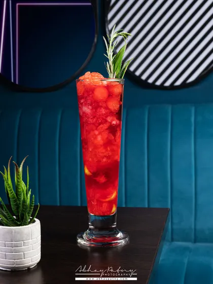 This mocktail shot uses the vibrant blue restaurant interior as a background. This not only creates a striking image but also ties the drink to the specific ambiance of the establishment.