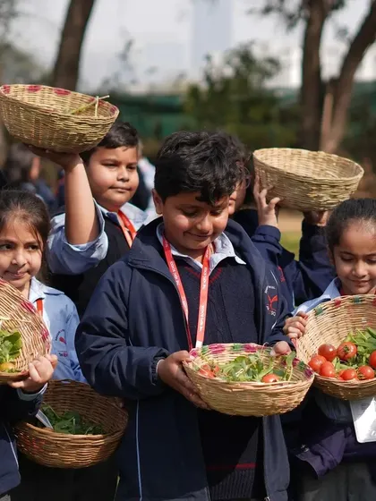 A group of school children holding up their baskets filled with freshly picked tomatoes and greens.