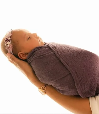 A mother's hands securely holding her swaddled newborn. This pose emphasizes how small and precious the baby is.