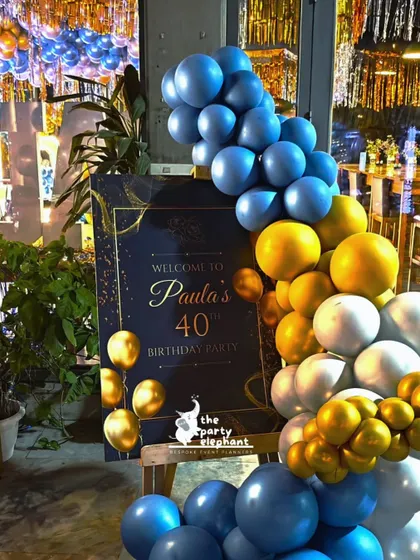 The welcome sign for Paula's 40th birthday was designed with an elegant blue and gold theme, framed by a beautiful balloon garland that matched the party's color scheme.