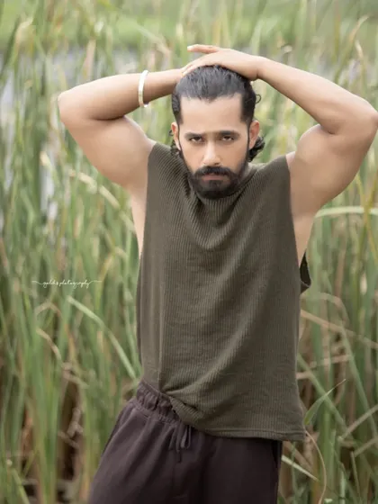 A black and white portrait of an actor in a natural, outdoor setting. The focus is on his strong physique and intense expression, creating a raw and powerful image.
