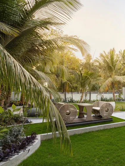 A dedicated seating nook at 'Tropical Manor', elevated slightly above the lawn. This space, framed by lush palm fronds, offers a private spot to enjoy the garden's serenity and the unique design of the outdoor furniture.