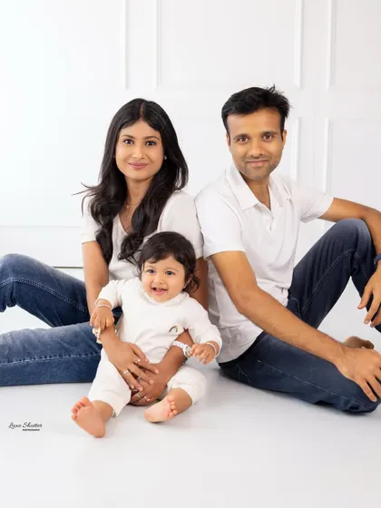 A casual and modern family portrait. The family is sitting on the floor in coordinating white tops and jeans, creating a relaxed and relatable image.