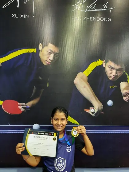Another shot of Varya with her gold medal and certificate from the district tournament. She stands in front of a poster of table tennis legends, a true inspiration for our future champs.