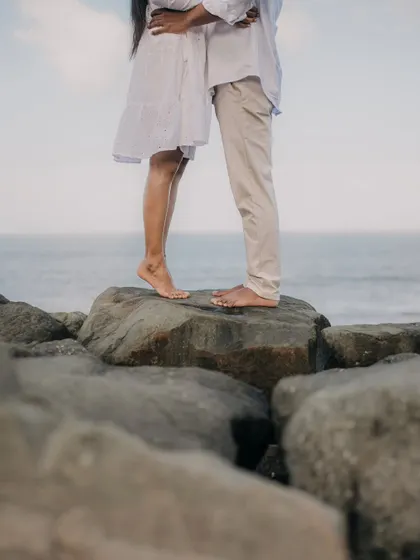 A detail shot focusing on the couple's feet as they stand together on a rock by the sea.
