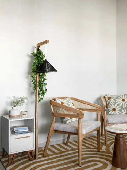 A cozy living room corner with wooden chairs, a small coffee table, and a unique floor lamp. The trailing vines add a touch of greenery.