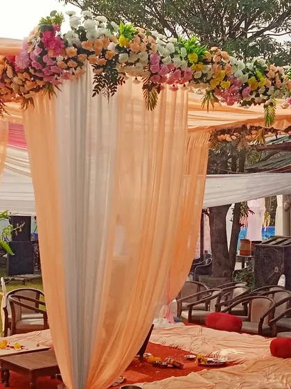 A simple and elegant mandap with peach and white fabric draping and a floral border, set up for a daytime garden wedding.