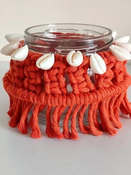 A close-up of the orange macrame jar with cowrie shell details.