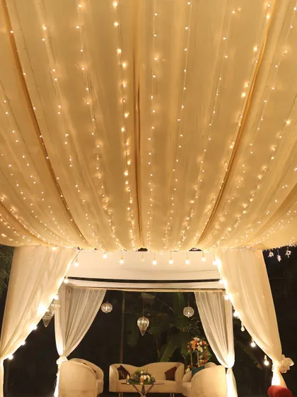 A romantic seating nook under a canopy of draped fabric and fairy lights, perfect for guests to relax and chat.