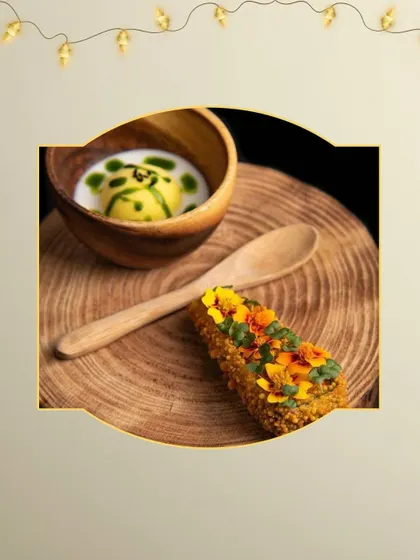 A modern take on Indian flavors. This appetizer pairs a crispy, garnished roll with a creamy soup shooter, served on a rustic wooden platter for a touch of earthy elegance.
