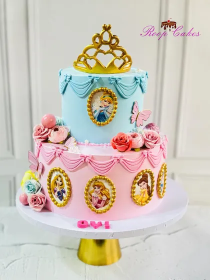 Where fairy tales and frosting come to life. This regal two-tier cake features portraits of Disney princesses in golden frames, topped with a beautiful tiara.