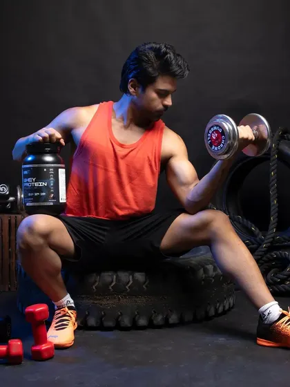 A male model performing a bicep curl with a dumbbell, with the whey protein product clearly visible. The shot emphasizes muscle definition and product effectiveness.