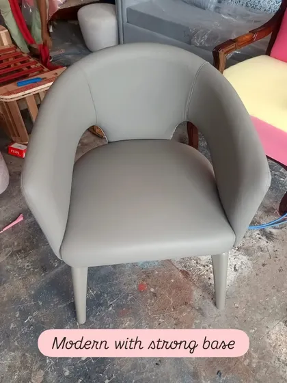 A modern accent chair with a strong base and a sleek, curved back. Upholstered in a smooth grey leatherette, this chair offers a minimalist aesthetic without sacrificing comfort or stability.