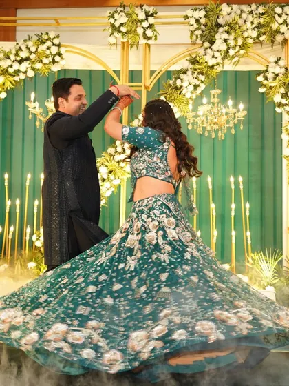 A candid moment of a couple dancing on their sangeet stage. The backdrop of green drapes, golden arches, and candle-like lights creates a romantic and dynamic setting for their first dance.