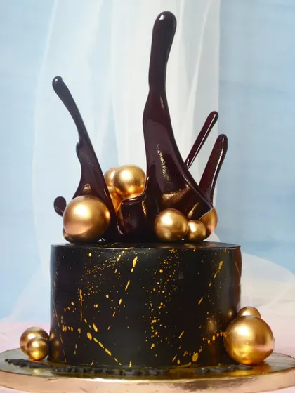 Absolute class. This black and gold cake features a dramatic chocolate splash topper, creating a modern and luxurious look for any celebration.