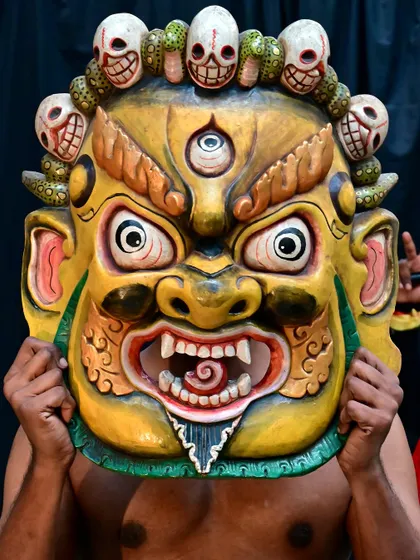 A yellow Nepalese evil eye warder mask, intricately carved and painted. Held up by a performer, its fierce expression is meant to keep evil-minded spirits at bay, making it a powerful guardian for your home.