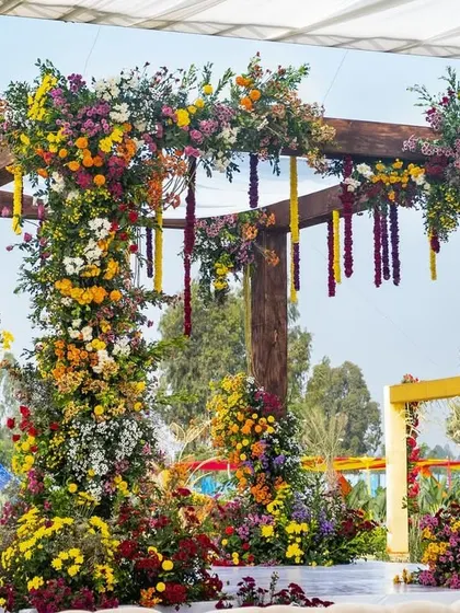 Another angle of the vibrant floral mandap, showing the hanging garlands and the lush arrangement against the clear blue sky.