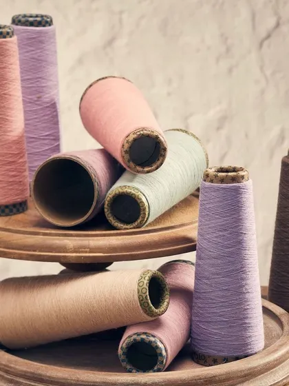 A collection of pastel-colored yarn cones arranged on a wooden tray. The soft lighting and gentle colors create a serene and beautiful image that highlights the material itself.