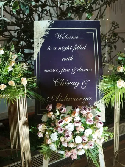 An elegant floral welcome sign for an evening reception, with beautiful bouquets of white and pastel roses on modern golden stands.