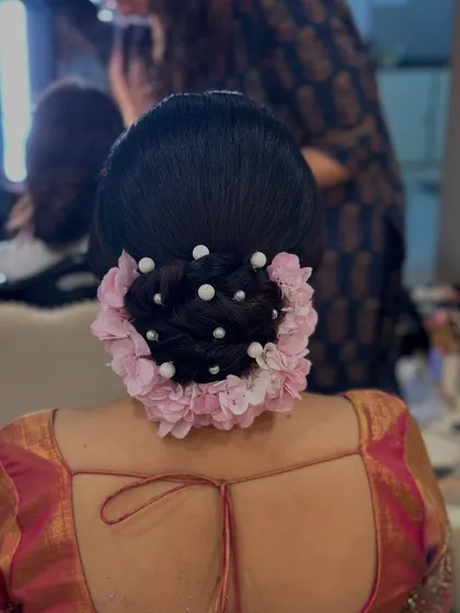 A close-up of the pink floral and pearl bun, showing the detail of the pearl pins scattered within the braided bun.