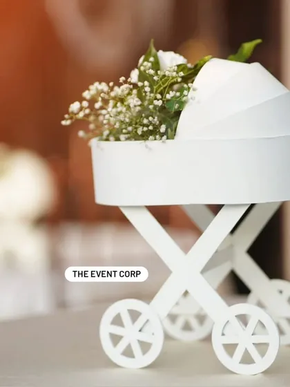 An adorable miniature baby carriage used as a centerpiece, holding a delicate bouquet of white flowers. A perfect, tiny detail for a baby shower.