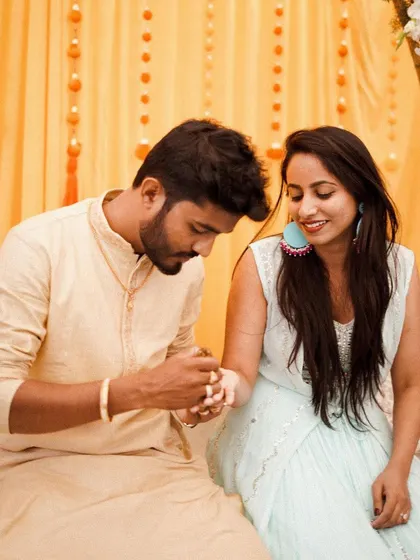 The couple shares a quiet moment during their Mehendi. The soft yellow background with floral details creates a warm and intimate setting.